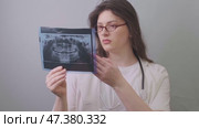 A dentist in a white coat holds an X-ray image, examining it carefully to detect possible dental pathologies. Стоковое видео, видеограф Svetlana Golovco / Фотобанк Лори