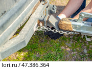 A man attaches a trailer to a car, securing safety chains to the trailer's hitch and drawbar. Стоковое фото, фотограф Коханова Наталья / Фотобанк Лори