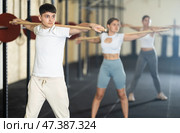 Young guy, together with other athletes, does a warm-up using a long stick in gym. Стоковое фото, фотограф Яков Филимонов / Фотобанк Лори