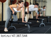 Athletic young woman pumping her biceps with a dumbbell while leaning on bench. Стоковое фото, фотограф Яков Филимонов / Фотобанк Лори
