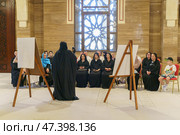 Manama, Bahrain - Jan 15 2024, An Arab woman dressed in a black burqa and niqab enthusiastically tells group of tourists about history of Islam inside of the Grand Mosque Al Fateh, Manama, Bahrain. Редакционное фото, фотограф Сергей Богомяко / Фотобанк Лори