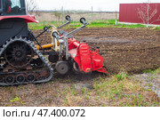 A tractor equipped with a red rotary cultivator actively prepares the soil in a rural field. The equipment loosens the earth, preparing it for planting and cultivation. Стоковое фото, фотограф Коханова Наталья / Фотобанк Лори