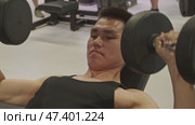 A young man in a black T-shirt is lifting weights in the gym, sweating from the effort. Стоковое видео, видеограф Strunov David / Фотобанк Лори