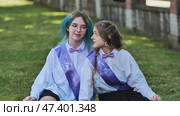 Two happy graduates wearing sashes are sitting on the grass and chatting on their last day of school. Стоковое фото, фотограф Mikhail Davidovich / Фотобанк Лори