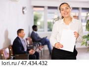 Friendly hostess woman stands at office reception with list of guests and expects invited visitors. Стоковое фото, фотограф Яков Филимонов / Фотобанк Лори