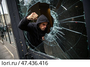 Man in black hoodie forcefully smashes glass door with clenched fist, vandalism, protest. Стоковое AI-изображение, AI-художник Коханова Наталья / Фотобанк Лори