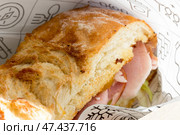Сэндвич с вкуснейшим свежим хлебом с хрустящей корочкой и ветчиной в оберточной бумаге и картонном подносе, купленный на фуд-корте. Стоковое фото, фотограф Татьяна Васильева / Фотобанк Лори