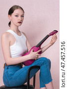 Woman holding ukulele tunes strings of musical instrument and looks at camera with blank expression. Стоковое фото, фотограф А. А. Пирагис / Фотобанк Лори