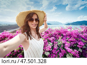 Woman in wide-brimmed straw hat travels alone Thailand, and takes a selfie against background of the Dam at Cheo lan Lan Lake in Khao Sok Park against the background of the reservoir, mountains and flowers at the observation point. Стоковое фото, фотограф Владимир Разгуляев / Фотобанк Лори
