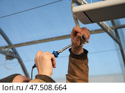 Installation of an infrared heater in the greenhouse. Maintenance of contacts of electrical wiring. A man with a wire and soldering iron in his hands. Стоковое фото, фотограф Роман Дзюбало / Фотобанк Лори