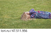 A little girl lies on the grass with her hands covering her face. Стоковое видео, видеограф Mikhail Davidovich / Фотобанк Лори