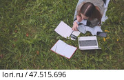 A young student with notebooks and a laptop lying on the grass. Стоковое видео, видеограф Mikhail Davidovich / Фотобанк Лори