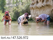 Три молодые женщины с фотокамерами снимают природу, стоя по колено в реке (2010 год). Редакционное фото, фотограф Snezka / Фотобанк Лори