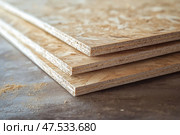 Layers of oriented strand board stacked on a wooden surface in workshop. Слои ориентированно-стружечной плиты, уложенные на деревянную поверхность в мастерской. Стоковое AI-изображение, AI-художник Katsiaryna Repich / Фотобанк Лори