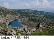 Summer day in low mountains. Stone hillsides, evergreen conifers, rocks in distance and emerald colored lake. Стоковое фото, фотограф Екатерина Якименко / Фотобанк Лори