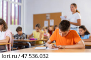Diligent tween boy making notes of teacher lecture in class. Стоковое фото, фотограф Яков Филимонов / Фотобанк Лори