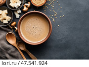A rustic clay bowl cradles rich miso soup, capturing Japanese culinary heritage. The umami-laden broth and earthy tones offer an inviting glimpse into traditional dining aesthetics. Стоковое AI-изображение, AI-художник Nart / Фотобанк Лори