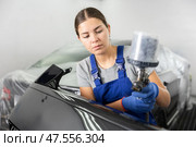 Car painting and automobile repair service. Woman in blue overalls paints car with airbrush pulverizer in paint chamber. Стоковое фото, фотограф Яков Филимонов / Фотобанк Лори