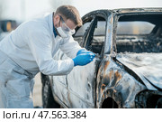 Forensic scientist examining burned car for evidence after fire incident. Стоковое AI-изображение, AI-художник Юрий Поздников / Фотобанк Лори