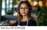 A friendly young woman with glasses stands in a cafe, dressed in an apron, exuding warmth and approachability in a bright atmosphere. Стоковое AI-изображение, AI-художник Данила Большаков / Фотобанк Лори