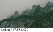 Dramatic mountain peaks covered in mist with green forests below under an overcast sky. Стоковое видео, видеограф Ольга Сухарева / Фотобанк Лори