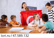 Cheerful young woman teacher demonstrating Turkish flag for schoolkids preteens during lesson of geography in auditory. Стоковое фото, фотограф Яков Филимонов / Фотобанк Лори
