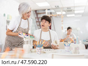 Experienced female ceramicist teaching enthusiastic guy to paint pottery. Стоковое фото, фотограф Яков Филимонов / Фотобанк Лори