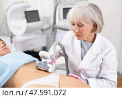 Young woman getting ultrasound cavitation body contouring treatment, anti-cellulite therapy, vacuum massage from old female cosmetologist. Hardware cosmetology for body sculpting. Стоковое фото, фотограф Яков Филимонов / Фотобанк Лори