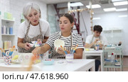 Positive enthusiastic senior woman offering guidance to interested young girl painting ceramic mug in pottery class. Creative hobby concept. Стоковое видео, видеограф Яков Филимонов / Фотобанк Лори