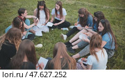 A group of female students are sitting in a circle on a meadow for collective work with notebooks. Стоковое видео, видеограф Mikhail Davidovich / Фотобанк Лори