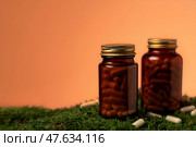Две стеклянные коричневые баночки с капсулами на зелёном мху, рядом рассыпаны белые капсулы. Стоковое фото, фотограф Anna Leeva / Фотобанк Лори