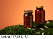 Две стеклянные коричневые баночки с капсулами на зелёном мху, рядом рассыпаны белые капсулы. Стоковое фото, фотограф Anna Leeva / Фотобанк Лори