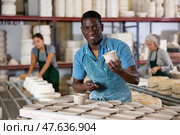 Positive man potter with new crafted crockry in workshop. Стоковое фото, фотограф Яков Филимонов / Фотобанк Лори