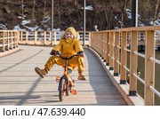 A cute boy in bright yellow clothes rides a bike. A happy child plays outside in early spring. Happy childhood. Стоковое фото, фотограф Photojuli / Фотобанк Лори