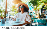 Serene cafe moment: Woman in wheelchair enjoys coffee with cheerful expression in sunlit outdoor setting, promoting inclusivity and positive attitude. Стоковое AI-изображение, AI-художник Данила Большаков / Фотобанк Лори