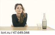 Beautiful young woman with distant expression sitting at a table with a wine bottle and empty glass on white background concept of loneliness hidden struggles and alcohol dependence. Красивая молодая женщина с отстраненным выражением лица сидит за столом с бутылкой вина и пустой бокал на белом фоне концепция одиночества скрытые борьбы и алкогольной зависимости. Стоковое AI-изображение, AI-художник Katsiaryna Repich / Фотобанк Лори