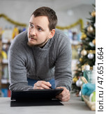 Middle-aged man restocking using tablet in store with New Year decoration. Стоковое фото, фотограф Яков Филимонов / Фотобанк Лори