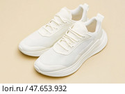 White leather lace-up running shoes with low tops, thick soles on a beige. The laces and rubber outsole. Sporty look. Men to wear during outdoor activities. Street hiking shoes. Trendy Male Boots Pair. Стоковое AI-изображение, AI-художник Марина Демидюк / Фотобанк Лори