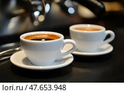 Two Espresso cups with coffee. Freshly brewed espresso shots on a dark wooden table with copy space, background, caffeine. Espresso cups, spoons, saucers. Refreshing hot cup of strong coffee at a cafe. Стоковое AI-изображение, AI-художник Марина Демидюк / Фотобанк Лори