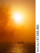 Doha, Qatar - Jan 08 2024, vertical aerial view of the sea where a tanker floats in the distance, the sky is covered with an orange mist through which the setting sun shines, at evening, Doha, Qatar. Стоковое фото, фотограф Сергей Богомяко / Фотобанк Лори