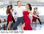 Smiling young woman in red dress and partner successfully perform mesmerizing movements of paso doble dance during dance party. Стоковое фото, фотограф Яков Филимонов / Фотобанк Лори