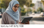 Female Muslim doctor in hijab, wearing scrubs and white coat, working with patient's records on digital tablet standing outside. Стоковое AI-видео, аниматор Ирина Старикова / Фотобанк Лори
