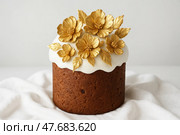 Пасхальный кулич с белой глазурью, украшенный золотыми  цветами из  мастики. Стоковое AI-изображение, AI-художник Башкирова Анна / Фотобанк Лори