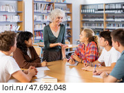 Portrait of adult female librarian and diligent schoolkids during classes in library. Стоковое фото, фотограф Яков Филимонов / Фотобанк Лори