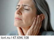 Elderly woman with gray hair holding her ears and expressing pain, with eyes closed and a tense facial expression. Concept of ear pain, hearing problems, tinnitus, or ear inflammation. The image is ideal for medical themes, healthcare, aging, and discomfort. Стоковое AI-изображение, AI-художник Анна Кривицкая / Фотобанк Лори
