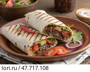 Вкусная шаверма, шаурма с аппетитным мясом, свежими овощами и зеленью, подаваемые на деревянной тарелке в неформальной обеденной зоне во время ланча. Стоковое AI-изображение, AI-художник Анна Сивакова / Фотобанк Лори