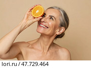 Smiling Mature Woman Joyfully Holding an Orange Slice Generative AI. Стоковое AI-изображение, AI-художник Roman Zavorotny / Фотобанк Лори
