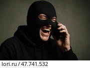 Мужчина в маске балаклаве. Телефонный мошенник разговаривает по телефону. Стоковое AI-изображение, AI-художник Башкирова Анна / Фотобанк Лори