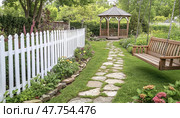 Swinging bench and gazebo decorating a peaceful garden with white fence. Стоковое AI-изображение, AI-художник Юрий Поздников / Фотобанк Лори
