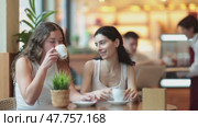 Two European women sitting at a table in a bright cafe, chatting and drinking hot coffee made from Arabica beans. Стоковое видео, видеограф Яков Филимонов / Фотобанк Лори